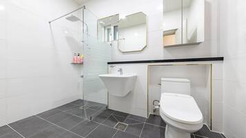 Un baño moderno con cabina de ducha de vidrio, un lavamanos blanco y un inodoro.