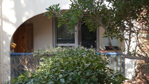 Un edificio con facciata bianca, una porta in legno e una finestra. Davanti all'edificio si trova un albero.