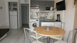 Una cucina compatta con forno a microonde, piano cottura e lavatrice. C'è un tavolo da pranzo con sedie e un televisore montato a parete.
