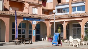 Un edificio con un cartel que dice 'CLUB DE PLONGÉE' y un cartel de 'PIZZA' en el exterior. Hay áreas de estar al aire libre con mesas y sillas.