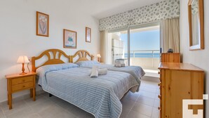 Un dormitorio con cama, mesitas de noche, cómoda y vista al mar.