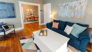 A living room with a blue sofa, a white coffee table, and a geometric rug. There is a painting on the wall and a door leading to another room. - Historic Revival Midtown Memphis Free Parking (Memphis)