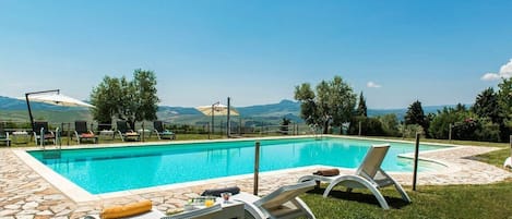 A rectangular swimming pool with a stone border, surrounded by lounge chairs and a stone patio.