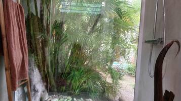 Un baño con puerta de vidrio que da a una vista tropical, ducha y banco de madera.