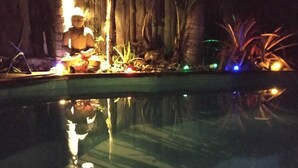 A nighttime pool area with a statue, plants, and ambient lighting. - BAS DE VILLA cosy, wooded garden with swimming pool, very quiet, town center. (Nouméa)