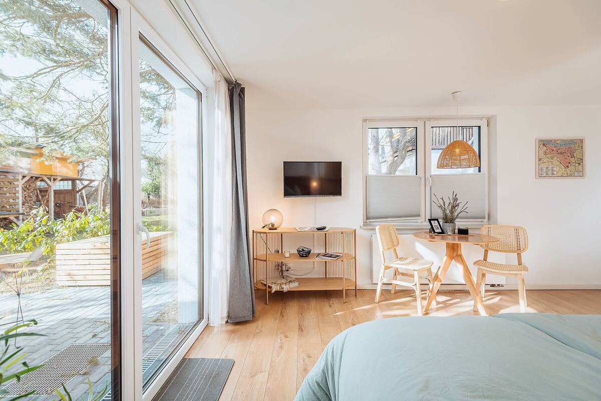 A bedroom with a bed, a desk with a TV, a window, and a view of the outdoors.
