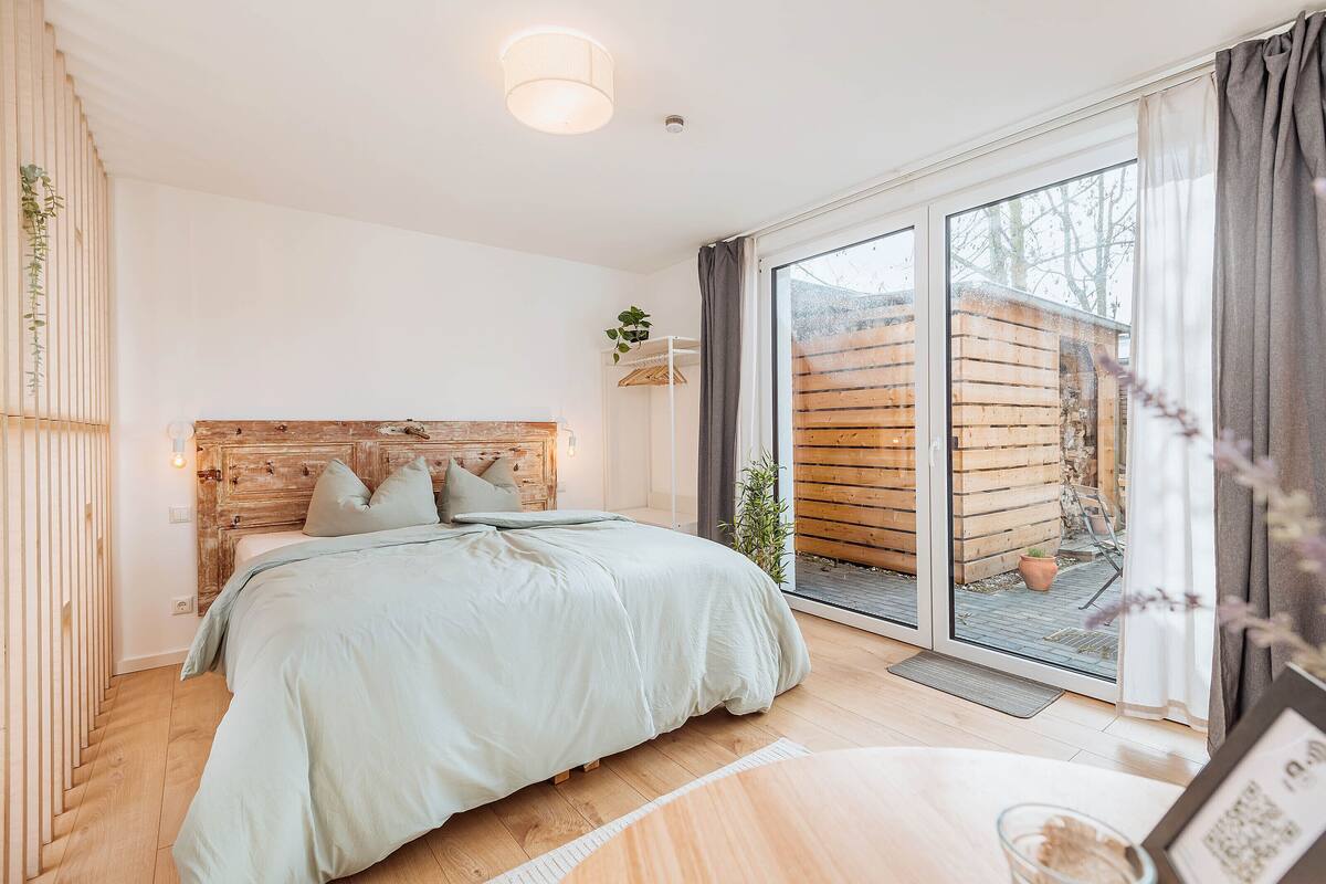 A bedroom with a wooden headboard, a large window, and a view of a wooden structure outside.