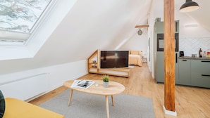 A modern loft apartment with a skylight, a cozy seating area with a TV, and a kitchen with green cabinets. - Apartments Kassebohmer Weg (Rostock)