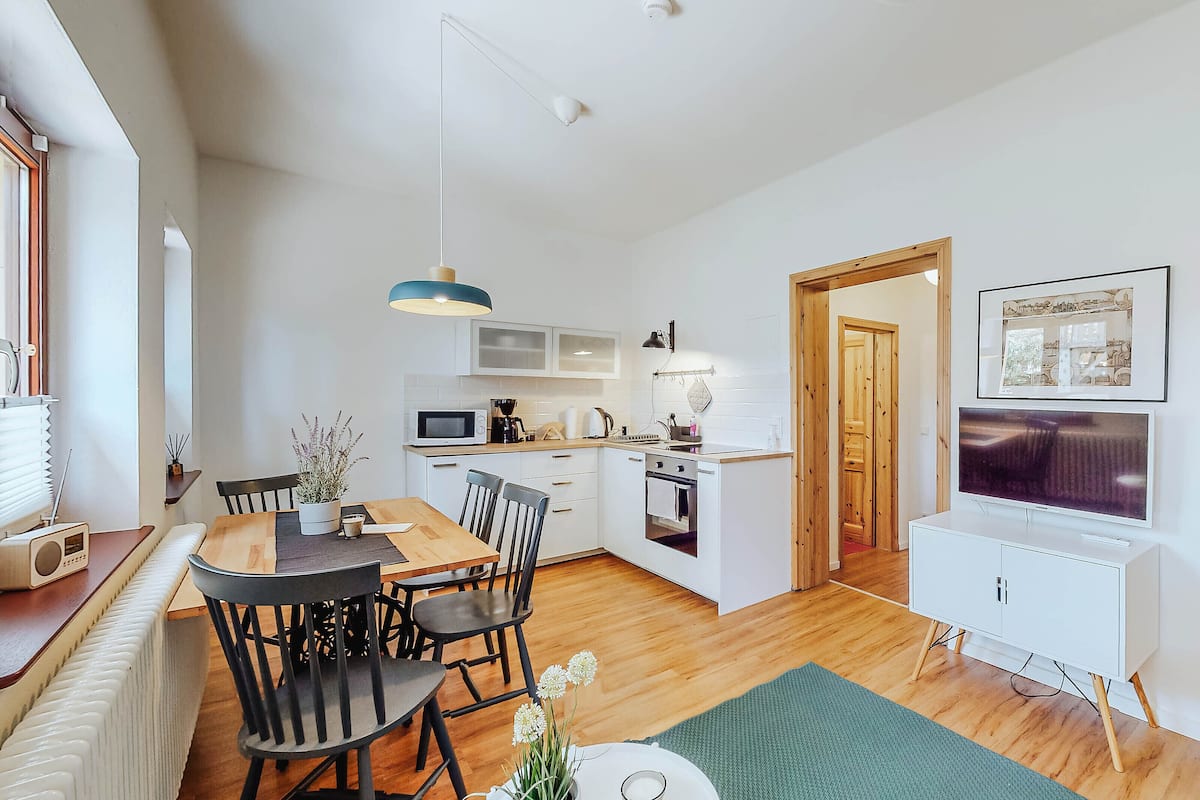 A modern kitchen with white cabinets, a microwave, and a stove. There is a dining area with a wooden table and chairs.