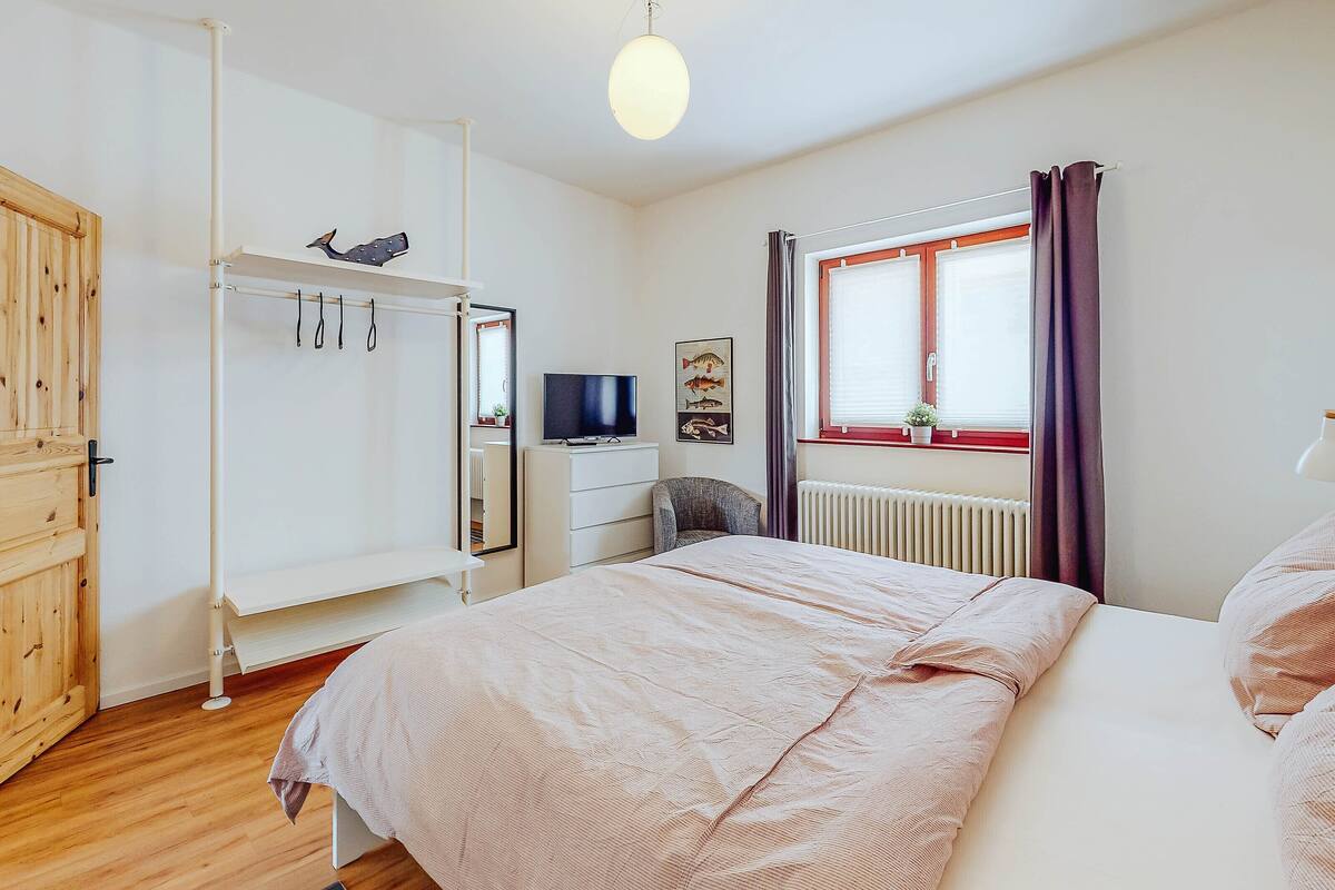 A bedroom with a bed, a TV, a wardrobe, and a window with curtains.