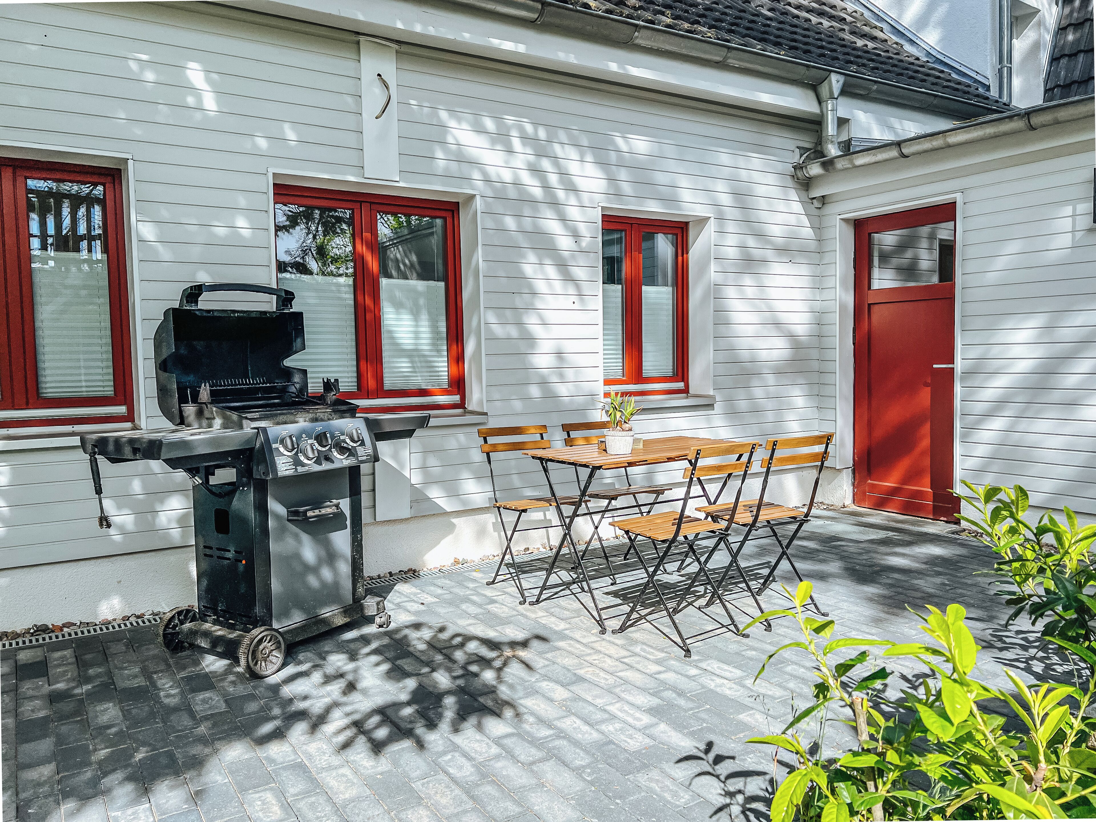 Une terrasse avec un barbecue, une table en bois et des chaises.