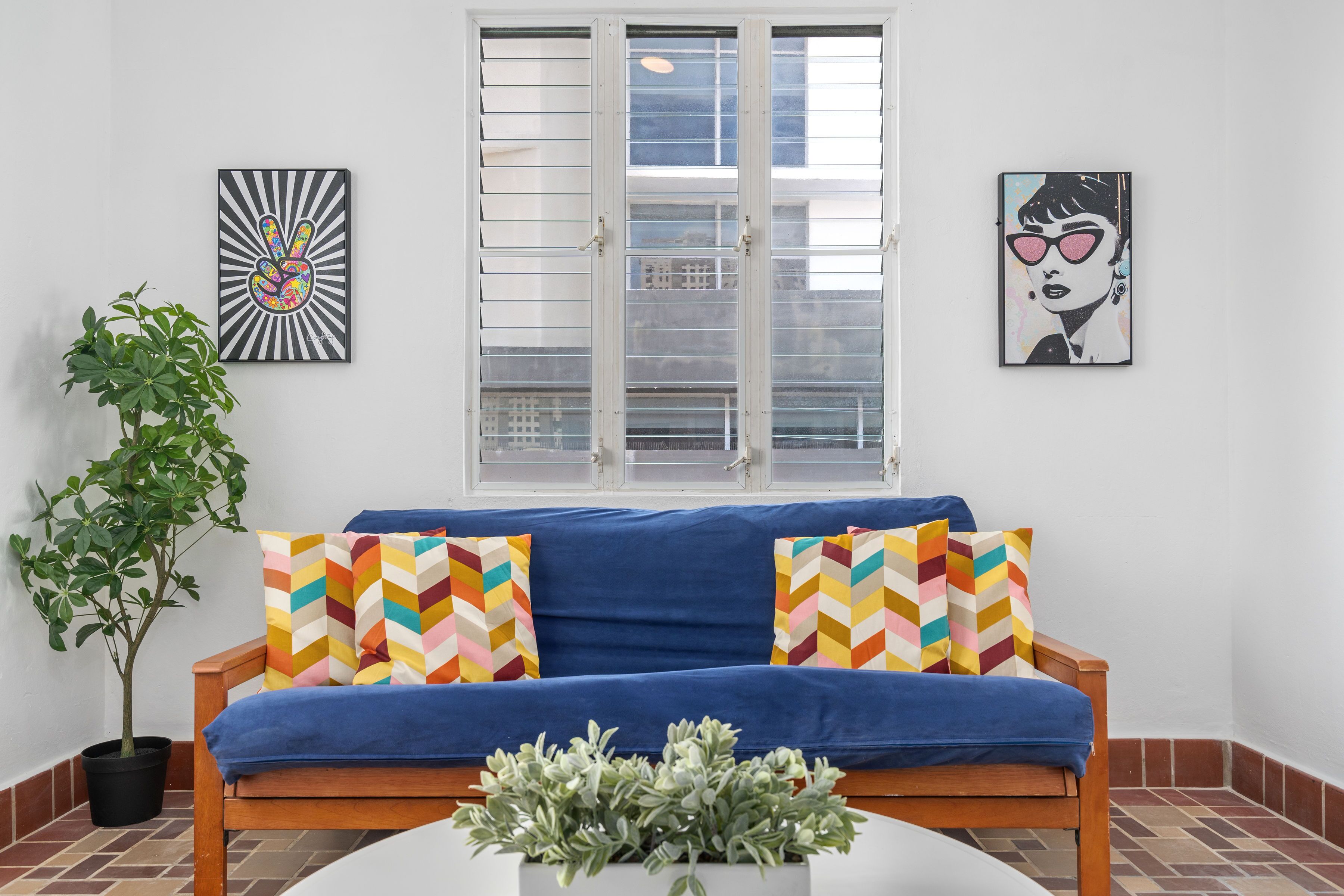 A room with a blue sofa, a potted plant, and two wall art pieces.
