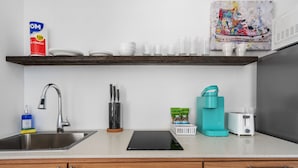 A modern kitchen with a stainless steel sink, a coffee maker, and a toaster. There are white plates and cups on the shelf above the sink. - Otium Rentals Plush King Bed Pacman Arcade (San Juan)