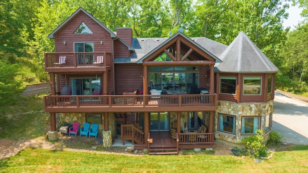 Une grande cabane en rondins à plusieurs étages, dotée d’un balcon, de fondations en pierre et de nombreuses fenêtres.