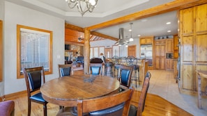 A spacious dining area with a wooden table and chairs, a chandelier, and wooden beams on the ceiling.