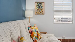 A bedroom with a bed, a colorful pillow, a wall-mounted lamp, and a window with blinds. - Otium Rentals San Juan City Apartment w Basketball Arcade (San Juan)