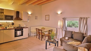 Una cocina acogedora con vigas de madera, un comedor con mesa y sillas, y una sala de estar con sofá y ventana.