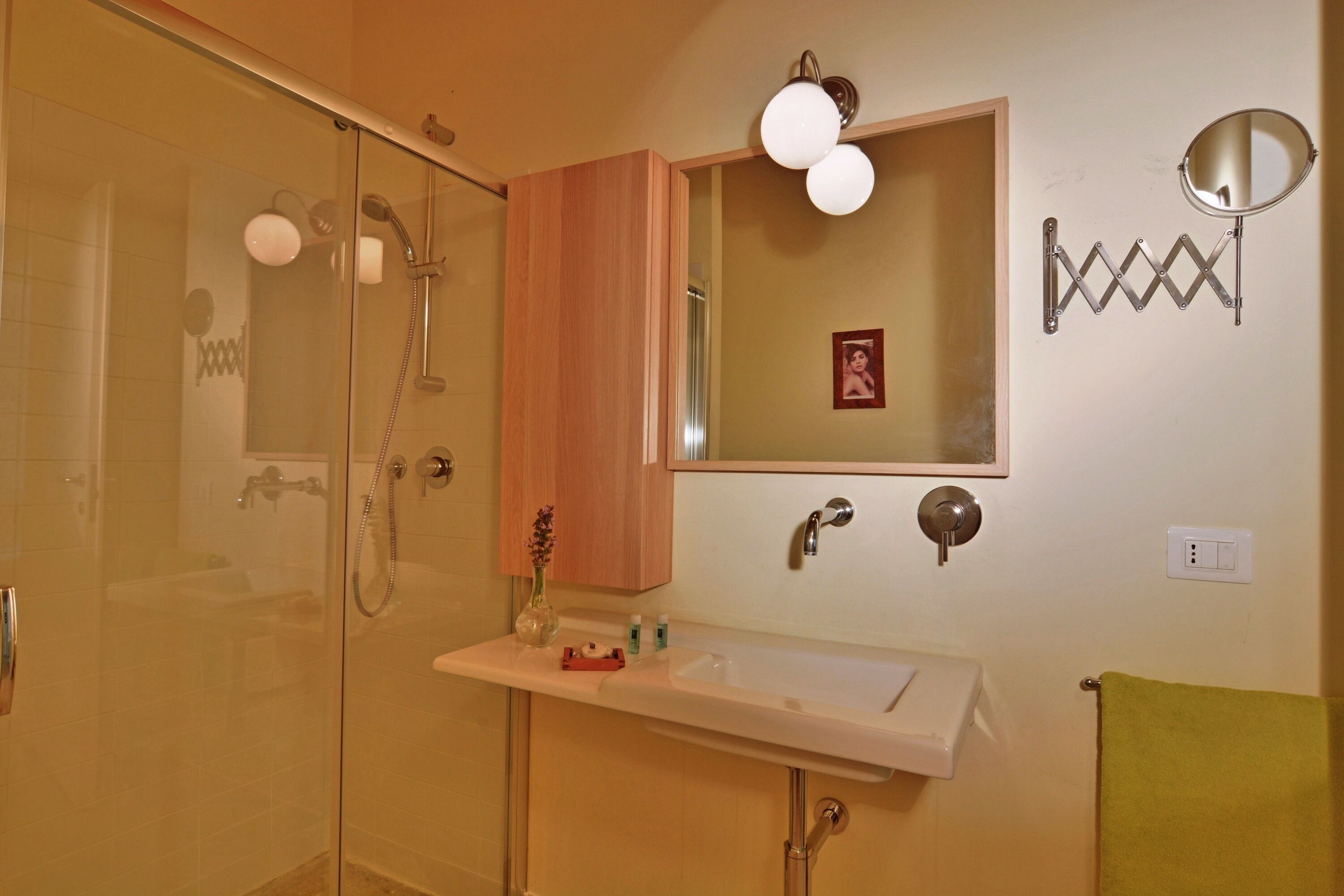 A bathroom with a glass shower enclosure, a sink with a mirror above it, and a towel rack.