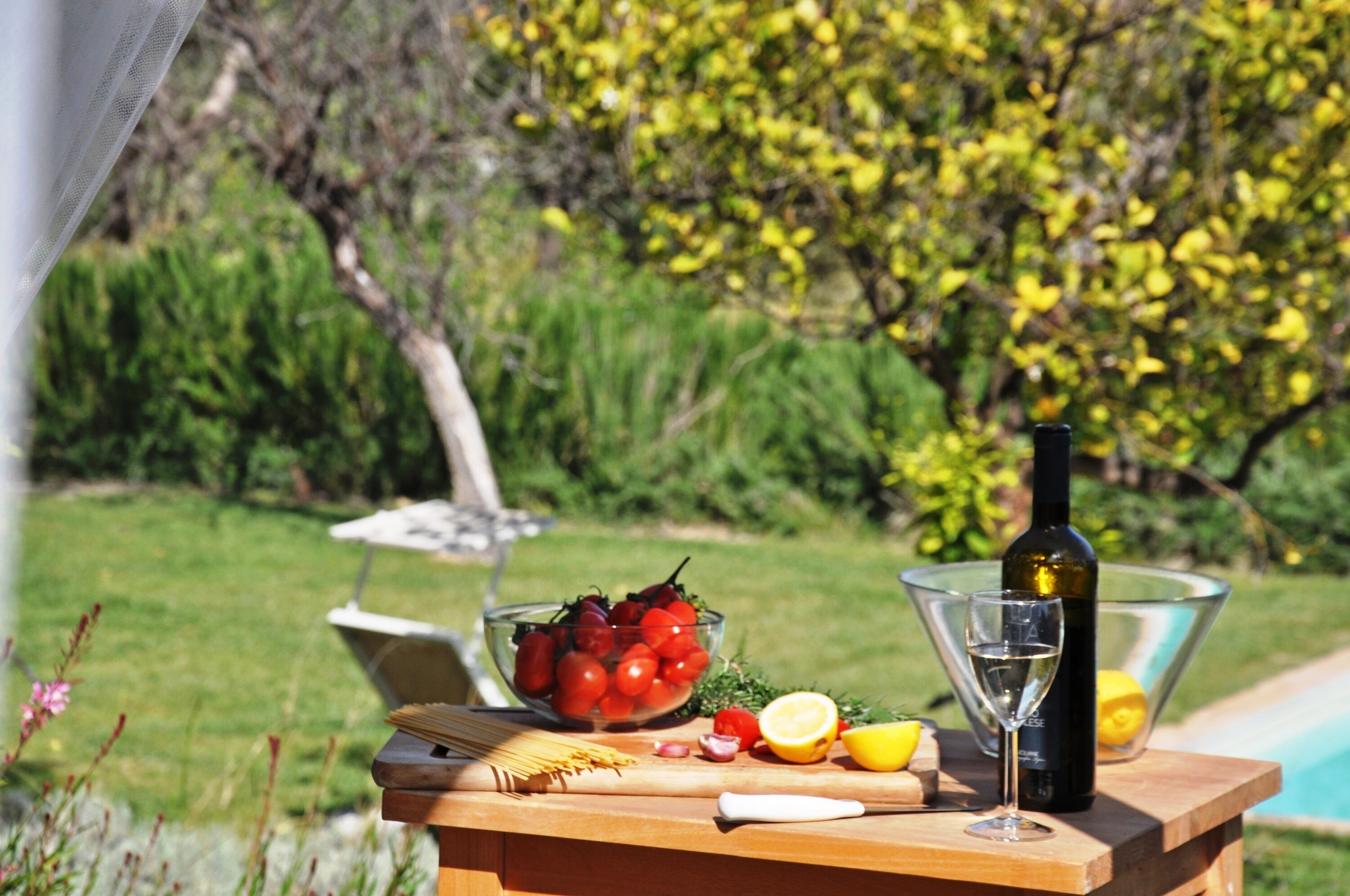 Una mesa de madera con un bol de tomates, una botella de vino, una copa y un limón.