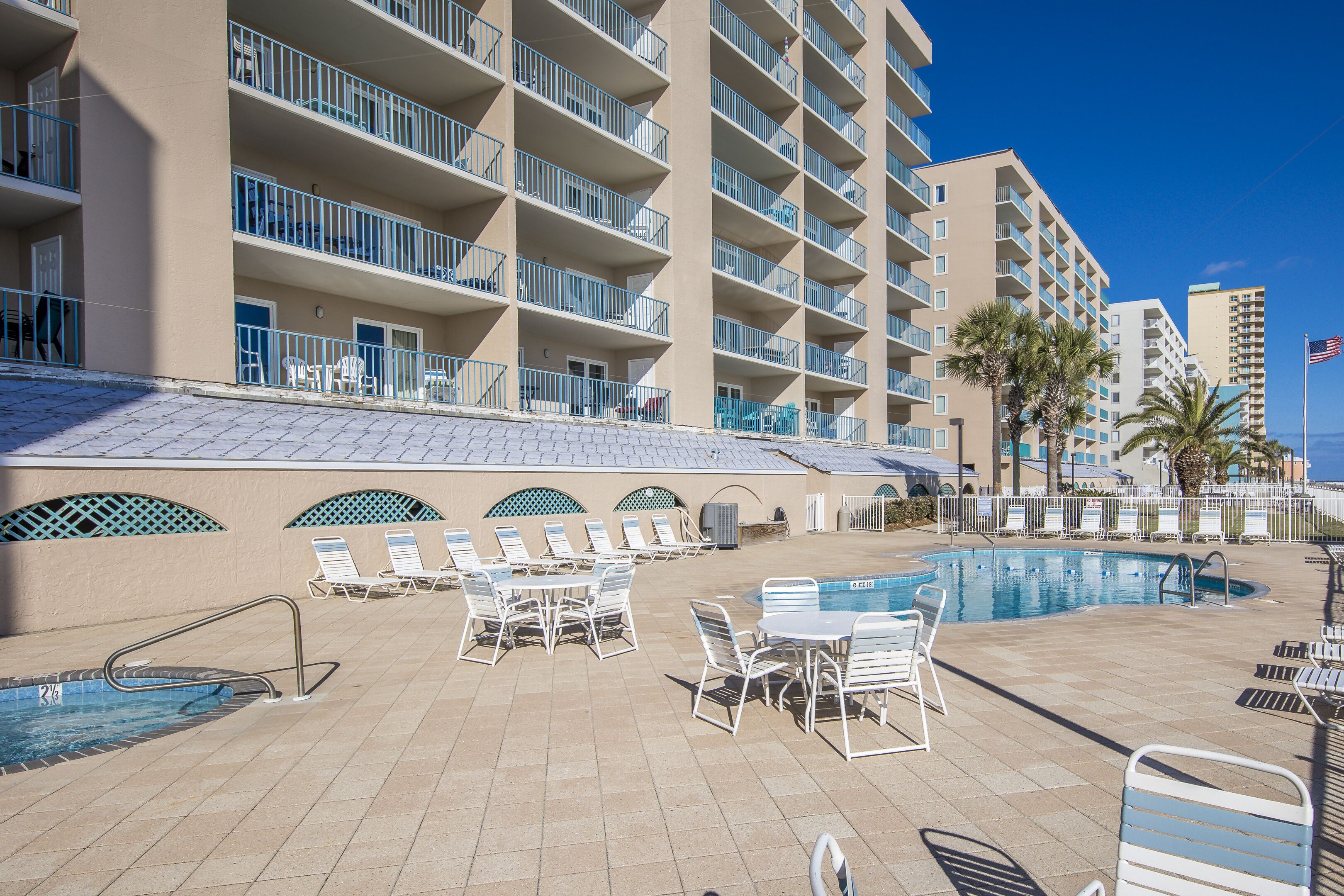 Zona de piscina en un resort con tumbonas, una piscina y un edificio con varios balcones.