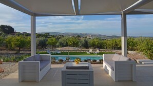 A covered outdoor seating area with a pool and vineyard views.
