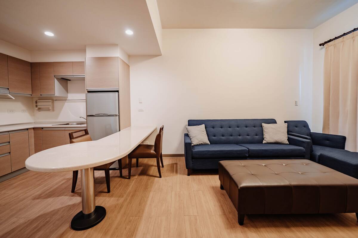A modern kitchen with a dining table and chairs, a sofa, and a small ottoman.