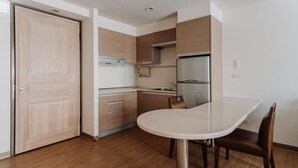 A modern kitchen with wooden cabinets, a stainless steel refrigerator, and a white dining table with a chair. - LAR Suite (Taichung)