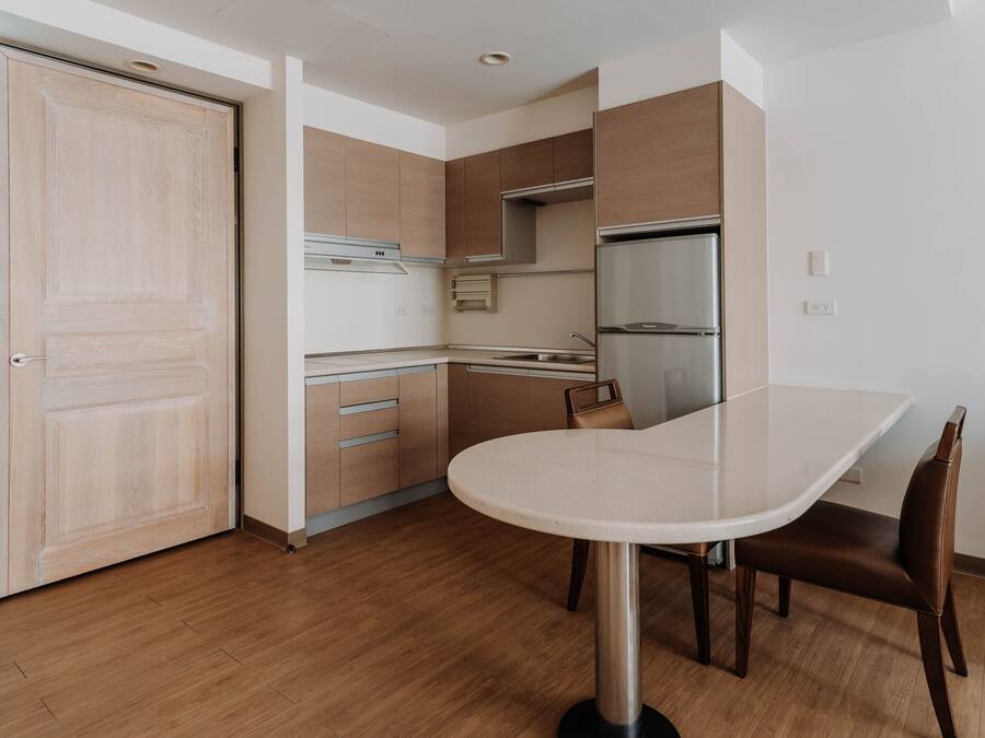 A modern kitchen with wooden cabinets, a stainless steel refrigerator, and a white dining table with a chair.