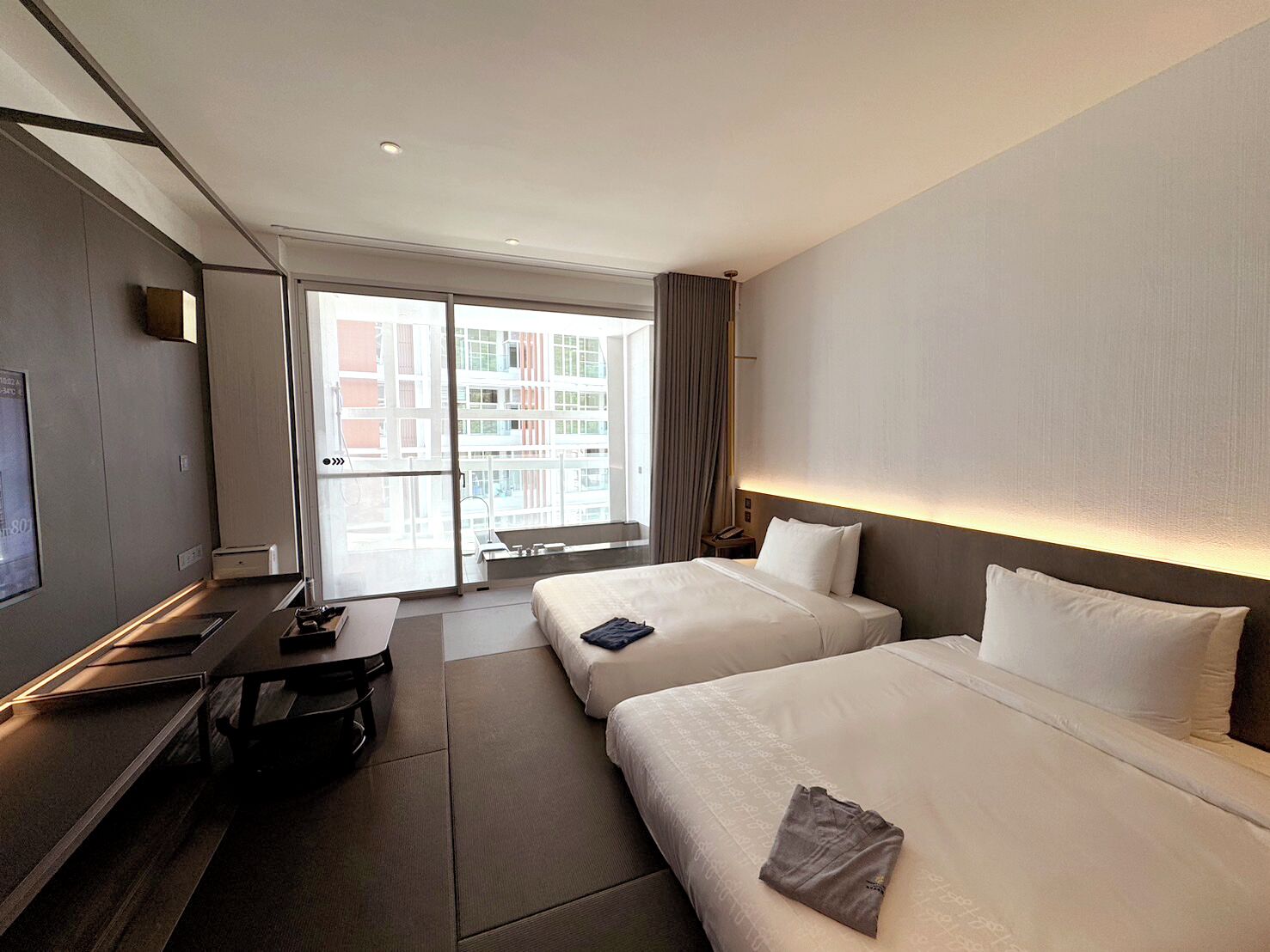 Une chambre d’hôtel avec deux lits, un bureau, une télévision et une grande fenêtre donnant sur des immeubles.