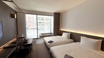 Une chambre d’hôtel avec deux lits, un bureau, une télévision et une grande fenêtre donnant sur des immeubles.