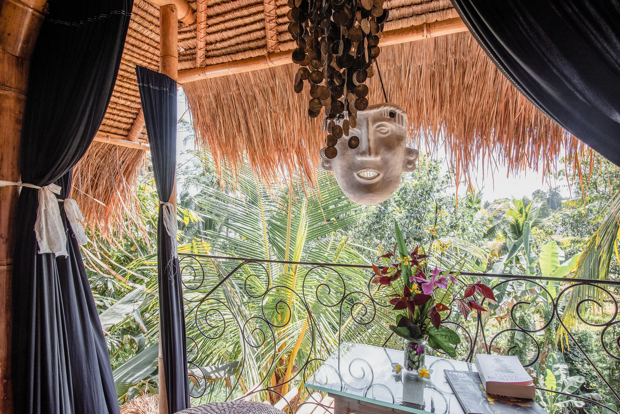 A room with a thatched roof, a hanging mask, and a view of lush greenery.
