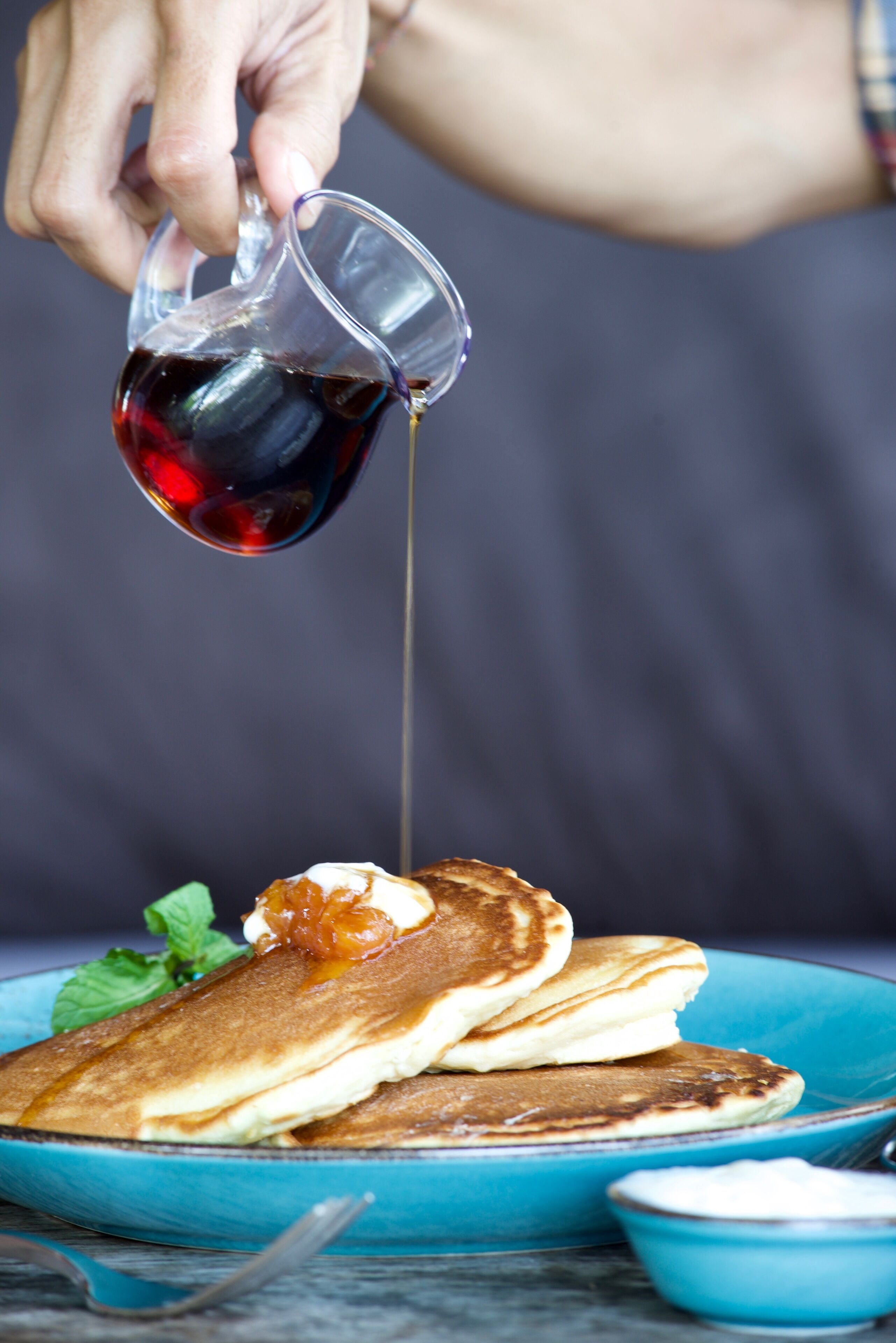 A hand pouring syrup over pancakes on a blue plate.