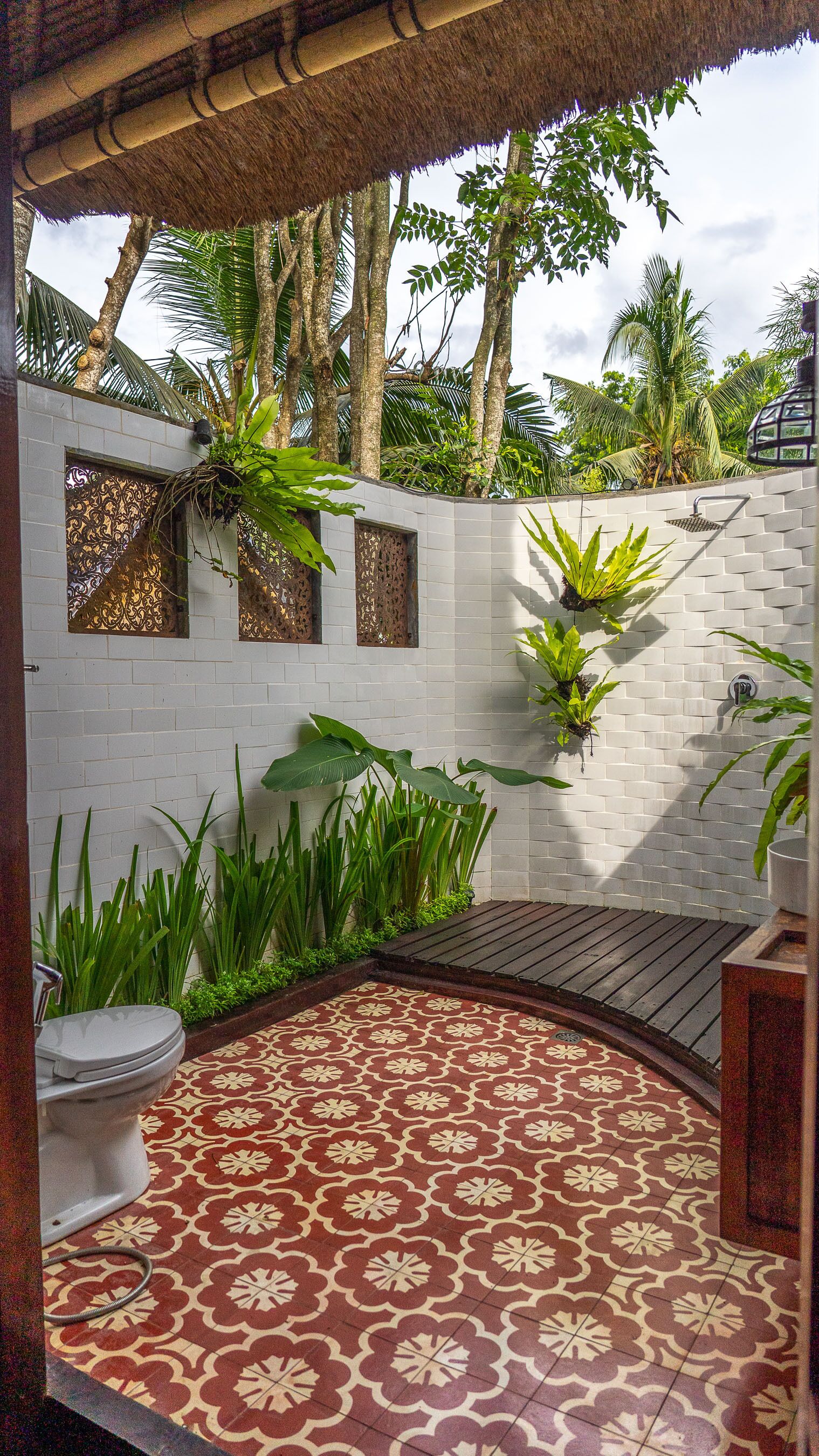 A bathroom with a patterned floor, a toilet, a shower area, and a wall with decorative panels and plants.