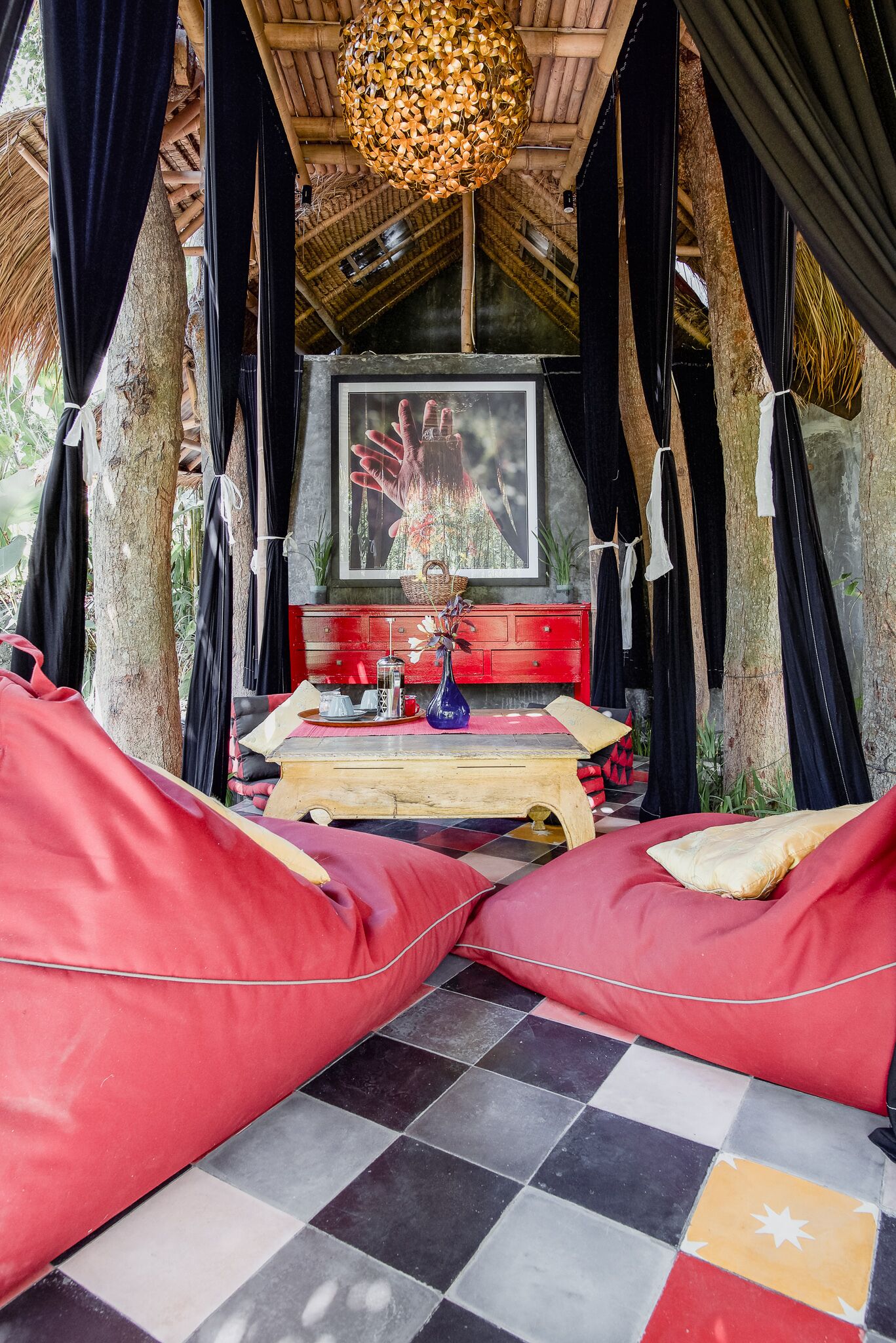 A cozy, rustic room with a checkered floor, a wooden table with a vase and a red cabinet, and two red bean bags.