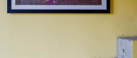 A framed artwork with a floral design and a pair of chopsticks on a yellow wall.