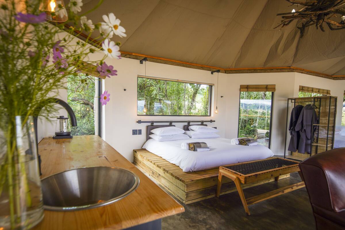 A bedroom with a wooden bed, a small table, a sink, and a window with a view of trees.