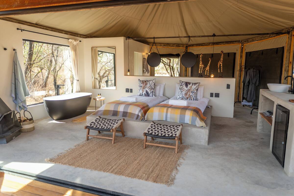 A spacious tented accommodation with a large bed, a bathtub, and a dining area.