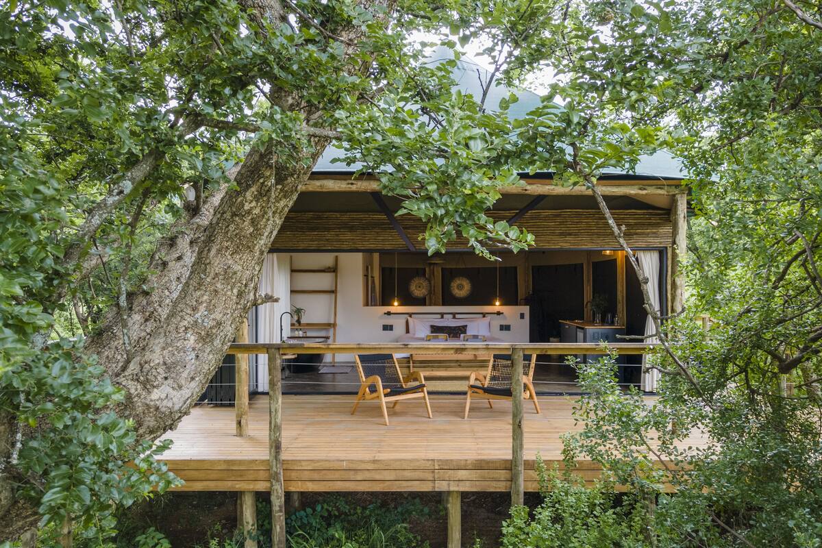 A wooden deck with two chairs, a dining table, and a kitchen area with a large window and a clock.