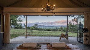 Un dormitorio con una cama grande, dos sillas, un ventilador y vistas a un paisaje con montañas y praderas.