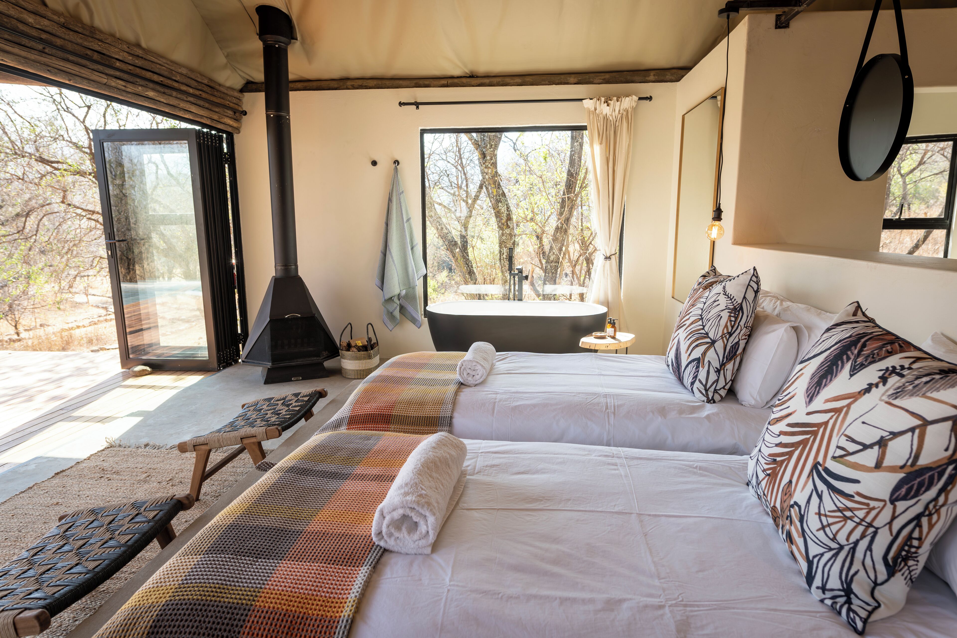 A bedroom with two beds, a large window, a fireplace, and a view of trees.