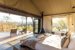 A bedroom with a large bed, a view of the outdoors, and a fireplace.