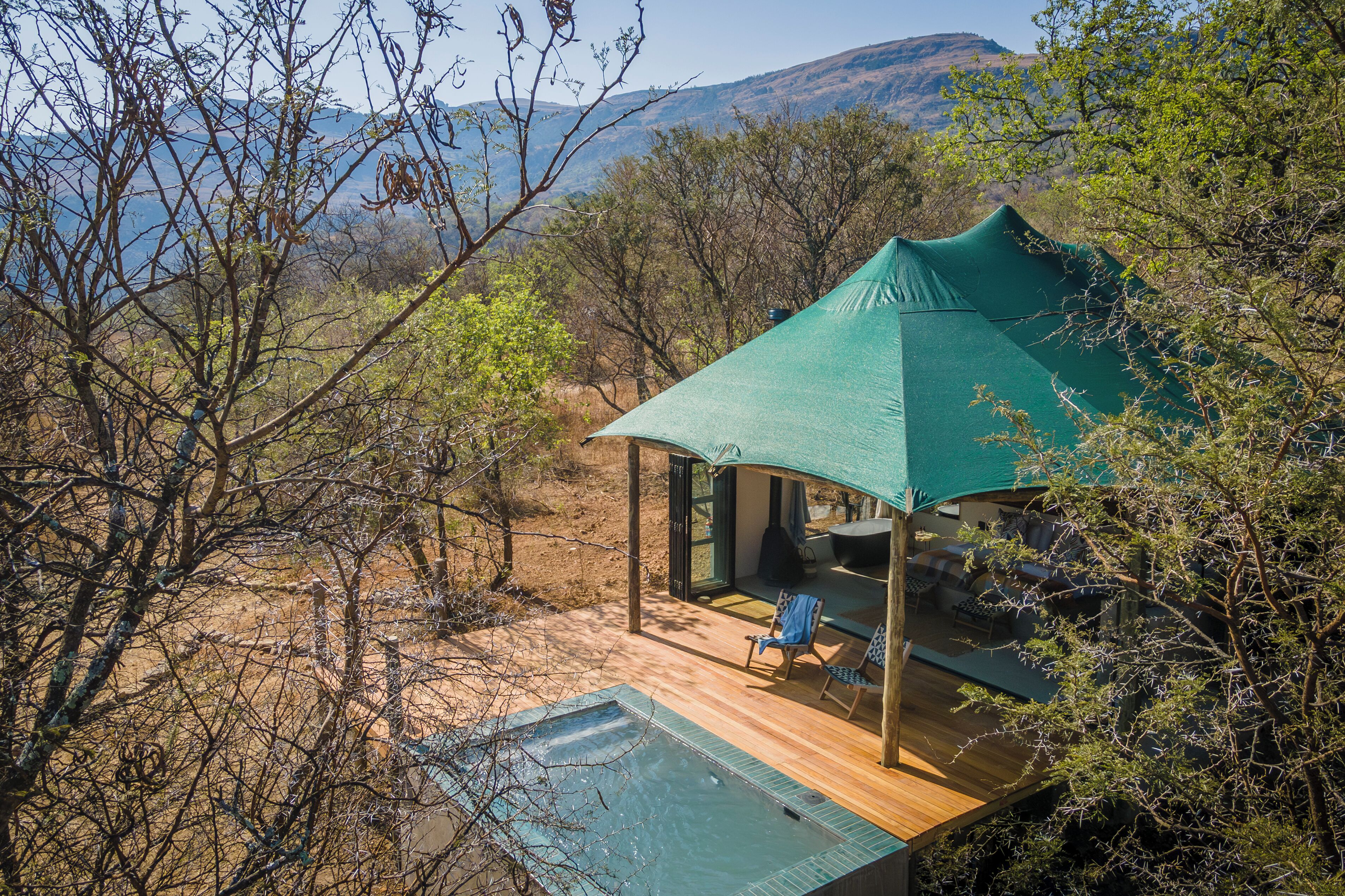 A secluded outdoor seating area with a pool, surrounded by natural vegetation and a mountainous backdrop.