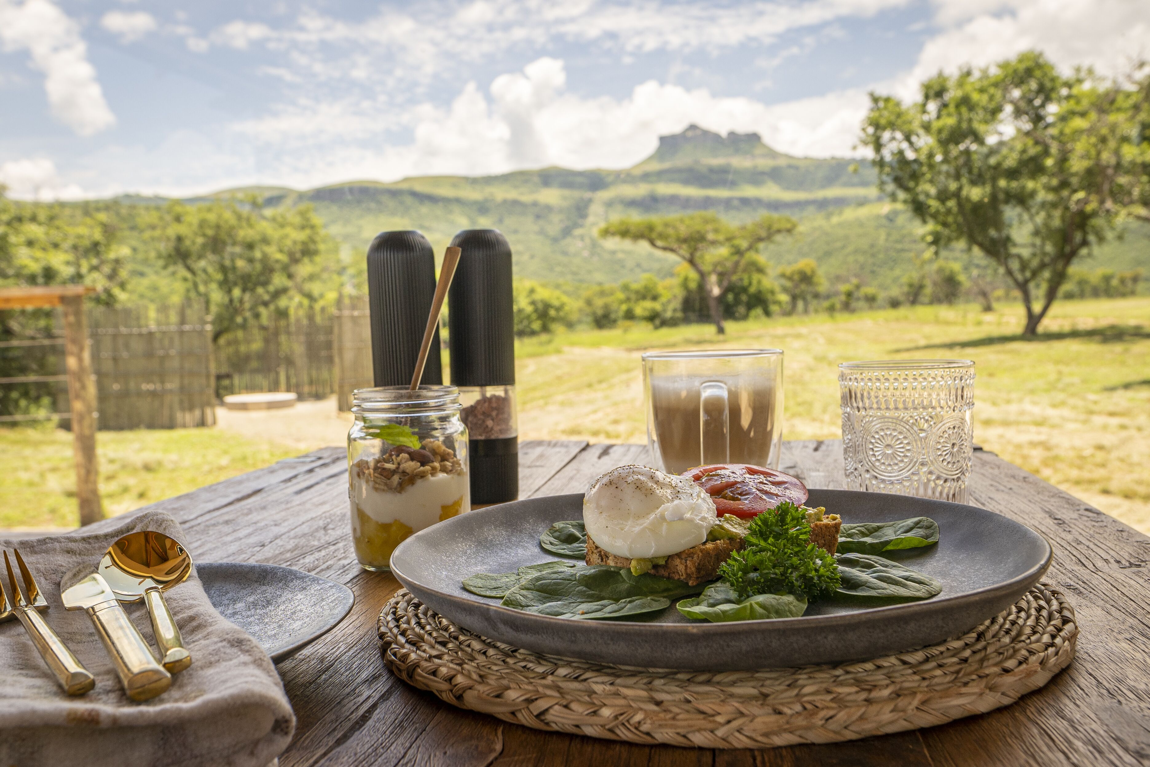 A meal set on a wooden table with a scenic view of green hills and trees in the background.