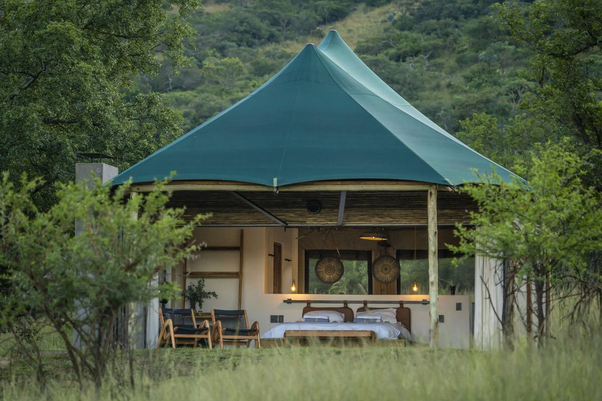 A single-story building with a green roof, a bed, and a chair in the foreground.