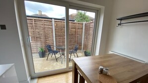 A modern kitchen with a wooden table, a sliding glass door leading to an outdoor patio with a table and chairs, and a small shelf above the table. - ⭐️Oxford⭐️ modern stylish apartment patio & parking (Oxford)