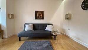 A modern living room with a dark sofa, two cushions, a small round table with a glass, and a Buddha statue on the wall. - ⭐️Oxford⭐️ modern stylish apartment patio & parking (Oxford)