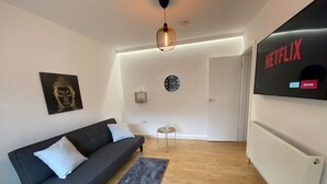 A modern living room with a black sofa, a small round table, a wall-mounted clock, and a Netflix sign. - ⭐️Oxford⭐️ modern stylish apartment patio & parking (Oxford)