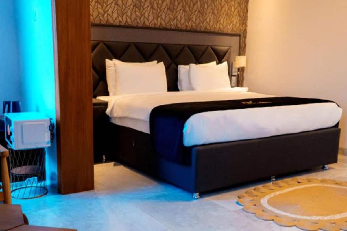 A modern hotel room with a large bed, a wooden chair, a small table, and a decorative rug.