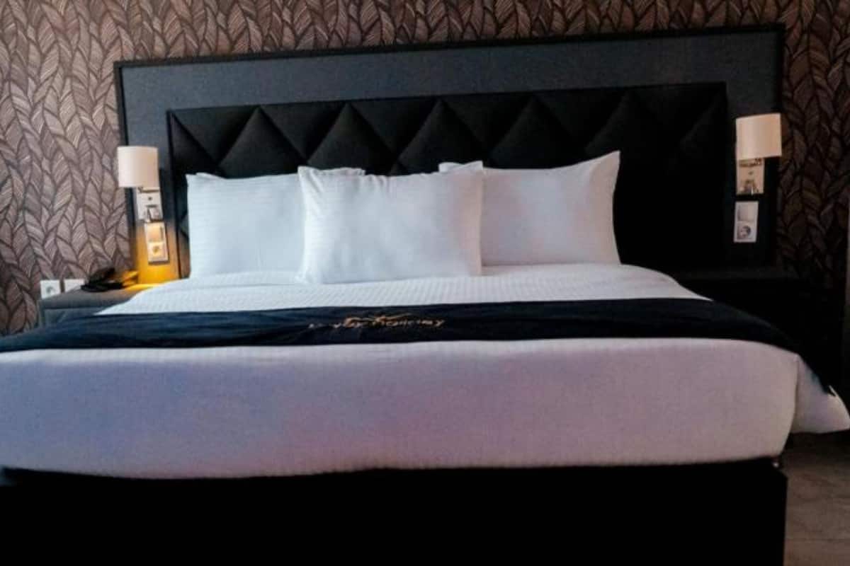 A neatly made bed with white linens, a black headboard, and two bedside lamps.