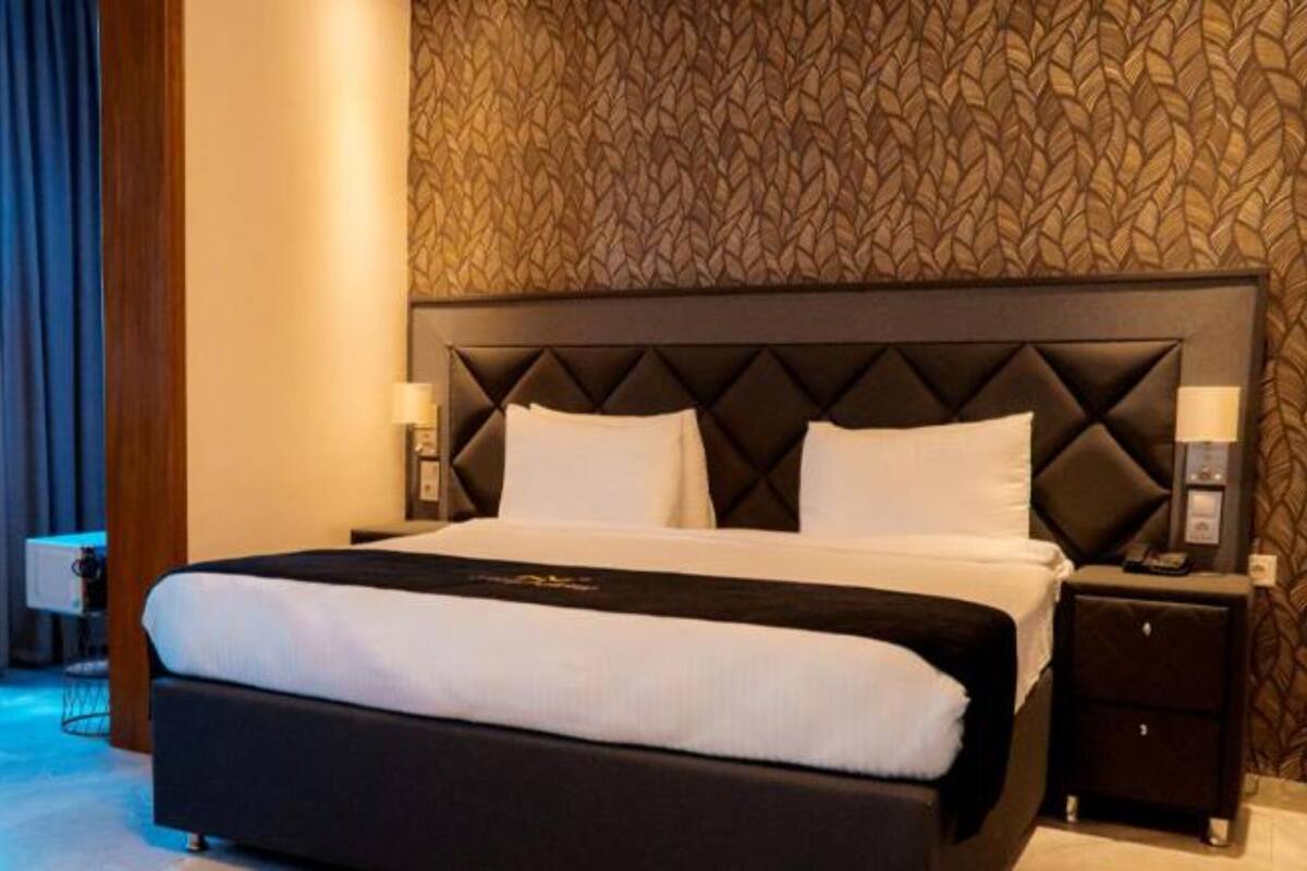 A hotel room with a large bed, a nightstand, a chair, and a patterned wall.